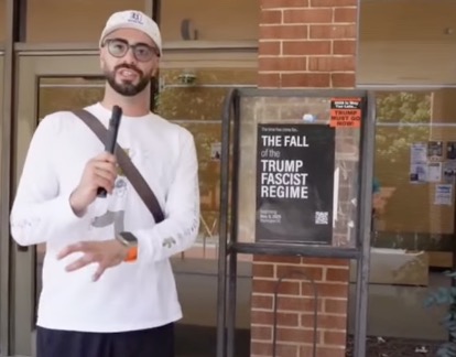 A man standing in front of a sign that says "The Fall of the Trump Fascist Regime"